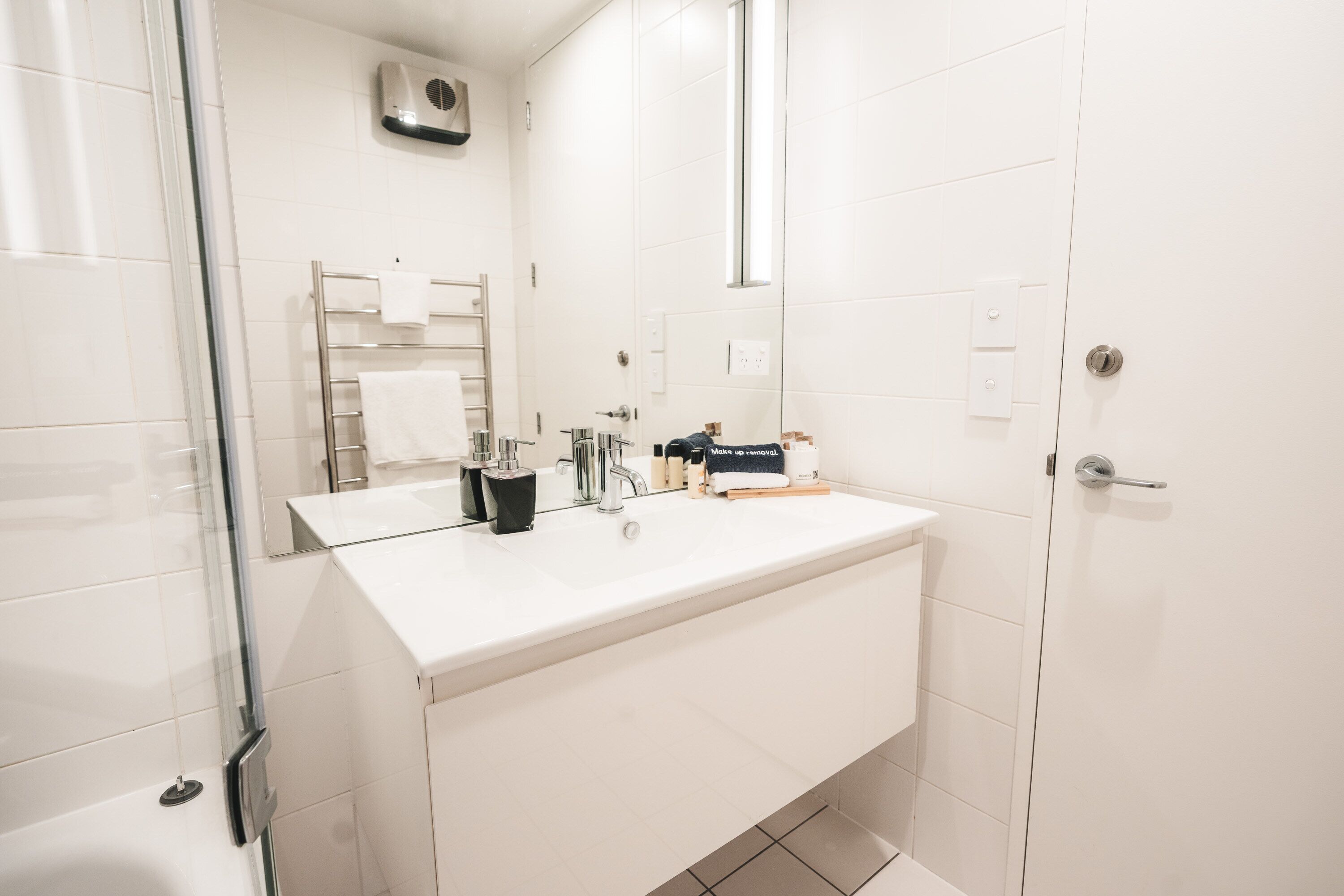 A modern bathroom with a white sink, mirror, and glass shower enclosure.