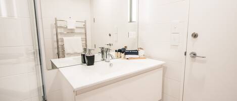 A modern bathroom with a white sink, mirror, and glass shower enclosure.
