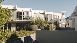 Una hilera de edificios modernos blancos con balcones, rodeados de vegetación y un cielo despejado.
