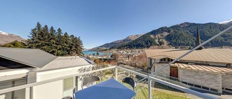 A balcony with a table and chairs overlooking a mountainous landscape and a body of water.