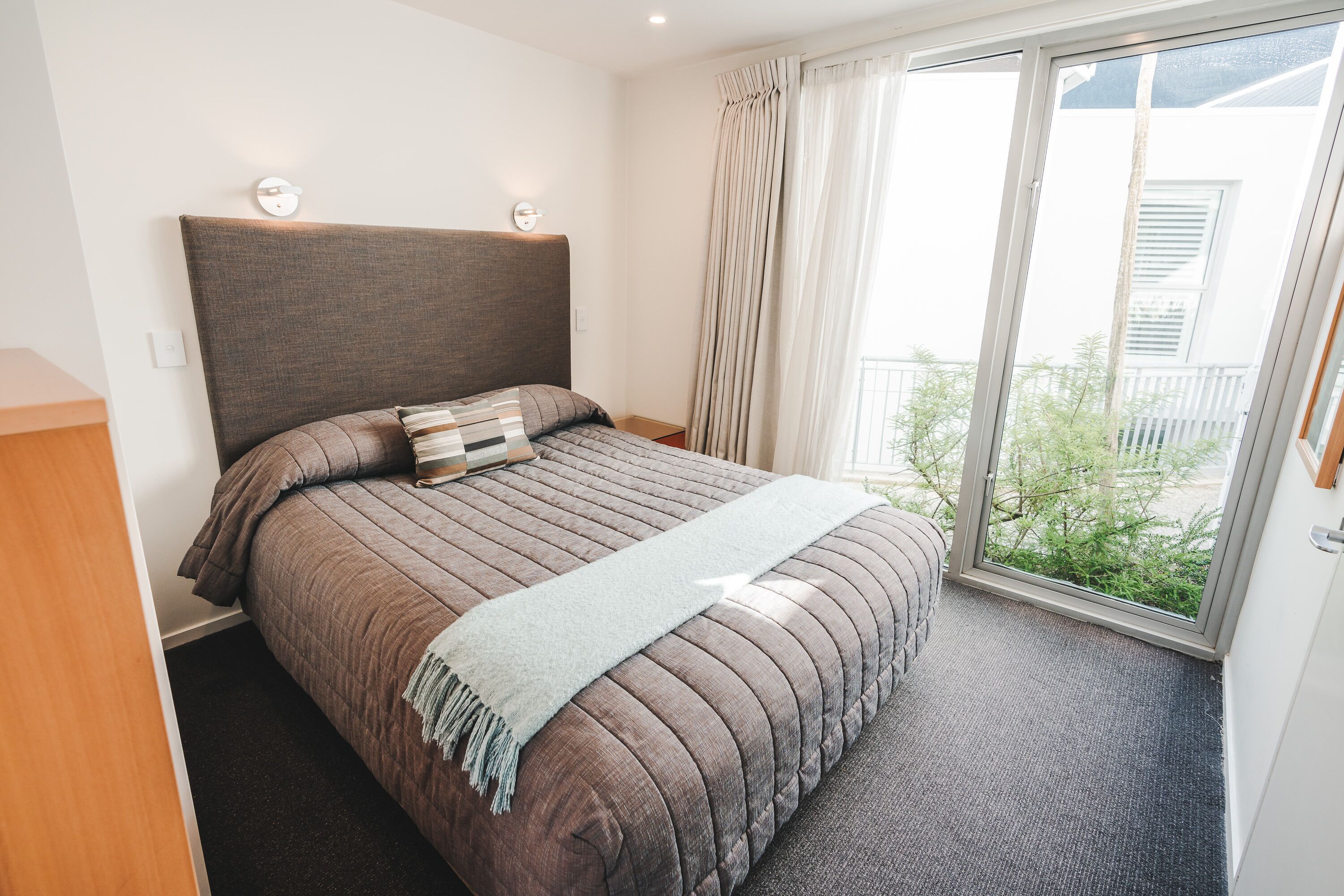 Quarto com cama grande, cabeceira, janela com cortinas e vista para o verde lá fora.