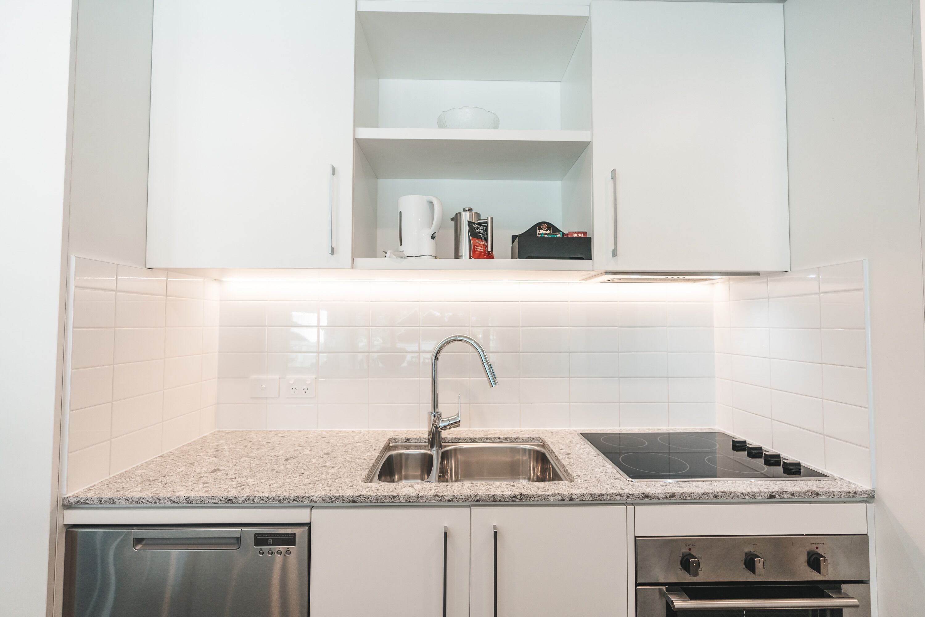 A modern kitchen with white cabinets, a stainless steel sink, a built-in stove, and a dishwasher.