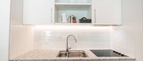 A modern kitchen with white cabinets, a stainless steel sink, a built-in stove, and a dishwasher.