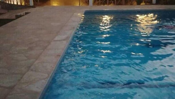 A swimming pool with a thatched roof structure in the background. - Queen K Cottages (Watamu)