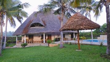A thatched-roof house with a pool and palm trees.