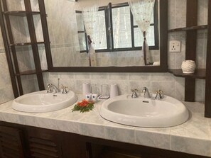 A bathroom with two sinks, a mirror, and a window with curtains. - Queen K Cottages (Watamu)