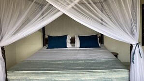 A bed with a canopy, two pillows, and a bedside table. - Queen K Cottages (Watamu)