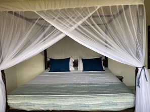 A bed with a canopy, two pillows, and a bedside table. - Queen K Cottages (Watamu)