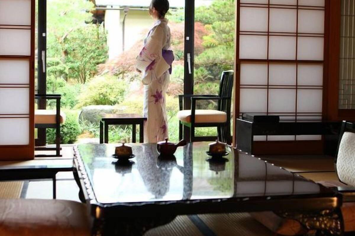 Una habitación japonesa tradicional con suelo de tatami, una mesa baja con juegos de té y puertas correderas que dan a un jardín.
