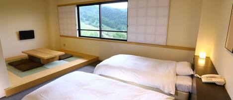 A hotel room with two beds, a small seating area, a window with a view of the mountains, and a bedside phone.