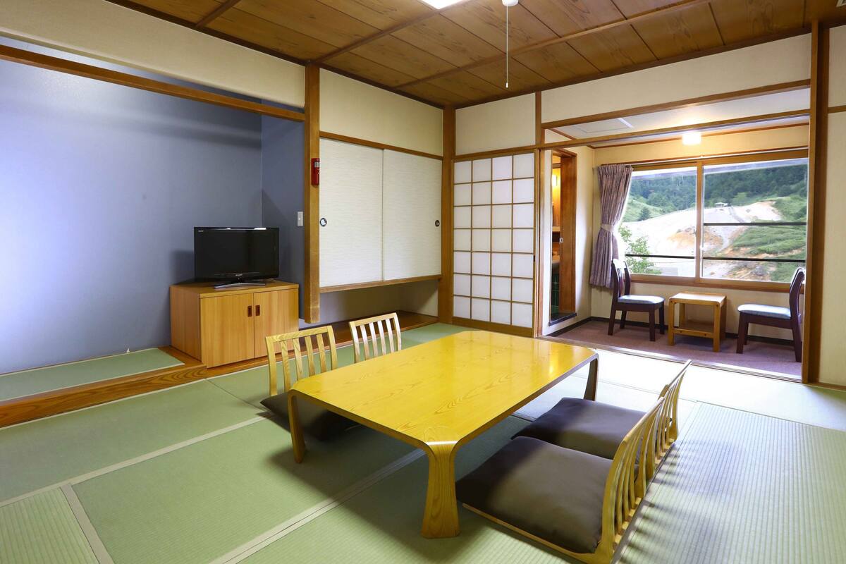 Um quarto japonês tradicional com tatames, uma mesa de madeira baixa e uma televisão em um móvel.