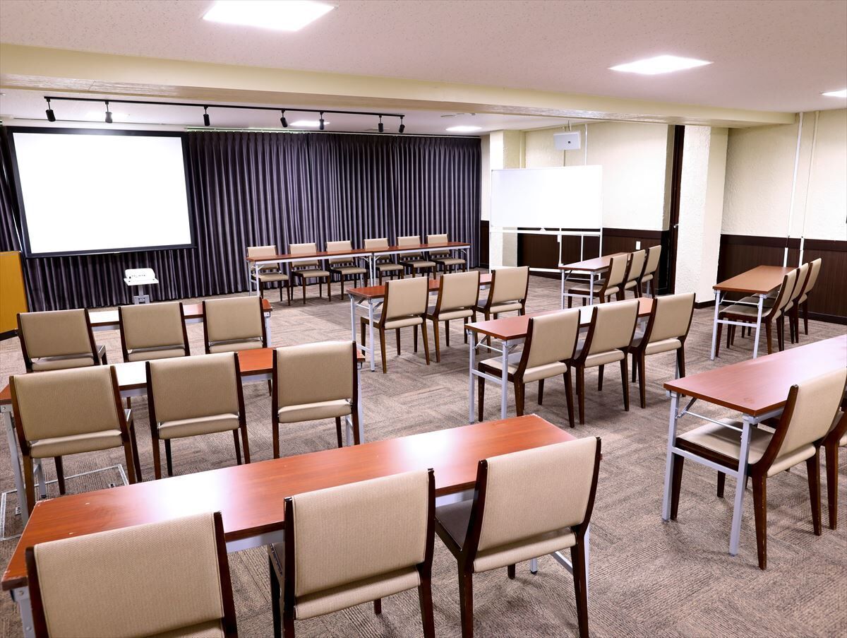 A conference room with multiple tables and chairs, a large screen, and a projector.