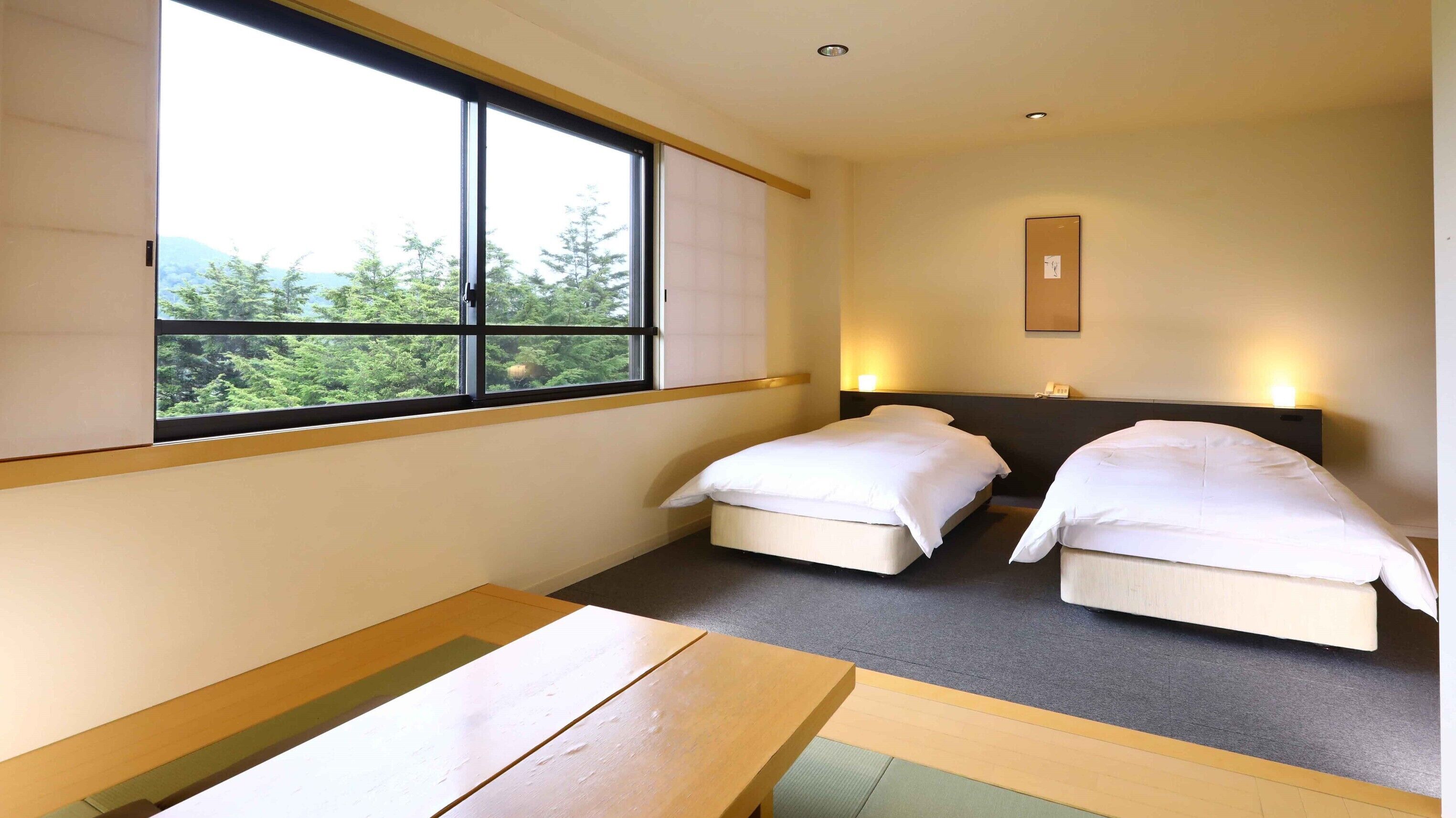Habitación de hotel con dos camas, una ventana con vista a vegetación, una mesita de noche y una lámpara de pared.