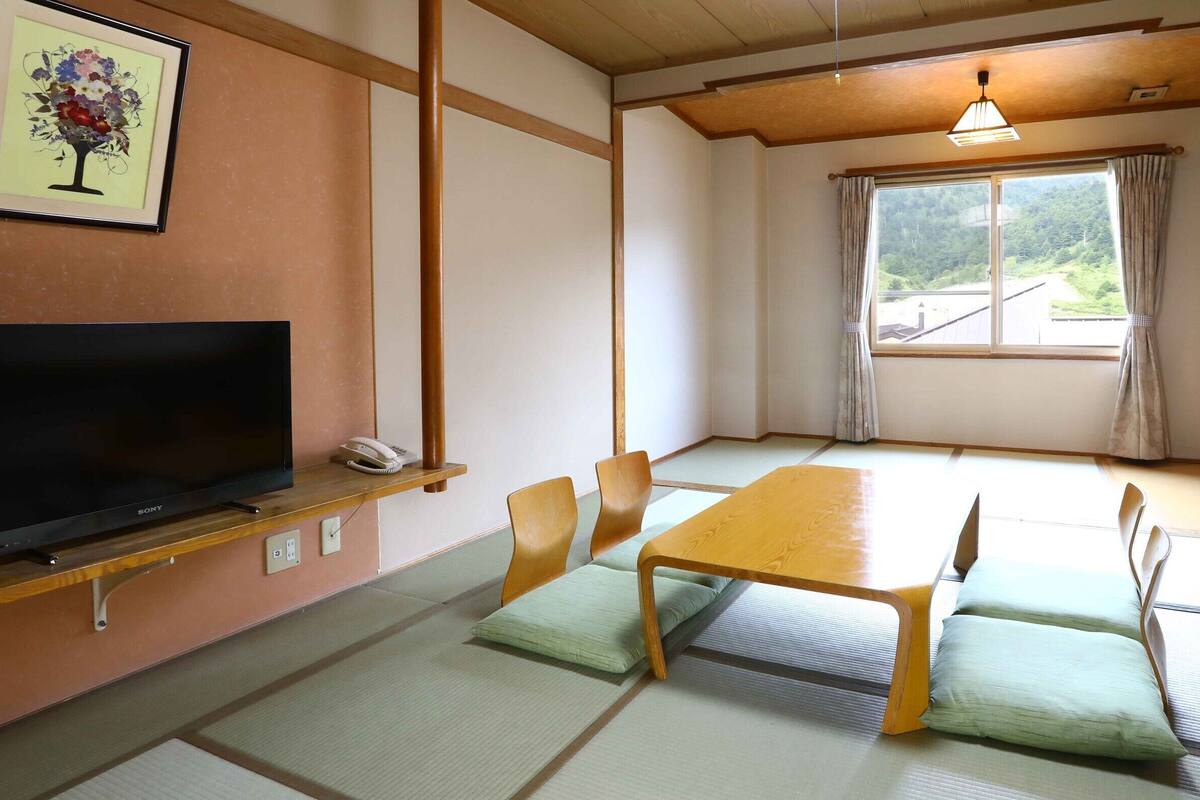Um quarto em estilo japonês tradicional, com tatames no chão, uma mesa baixa e uma televisão em uma estante.