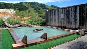Zona de aguas termales con cerca de madera, una piscina y vistas a una ladera verde.