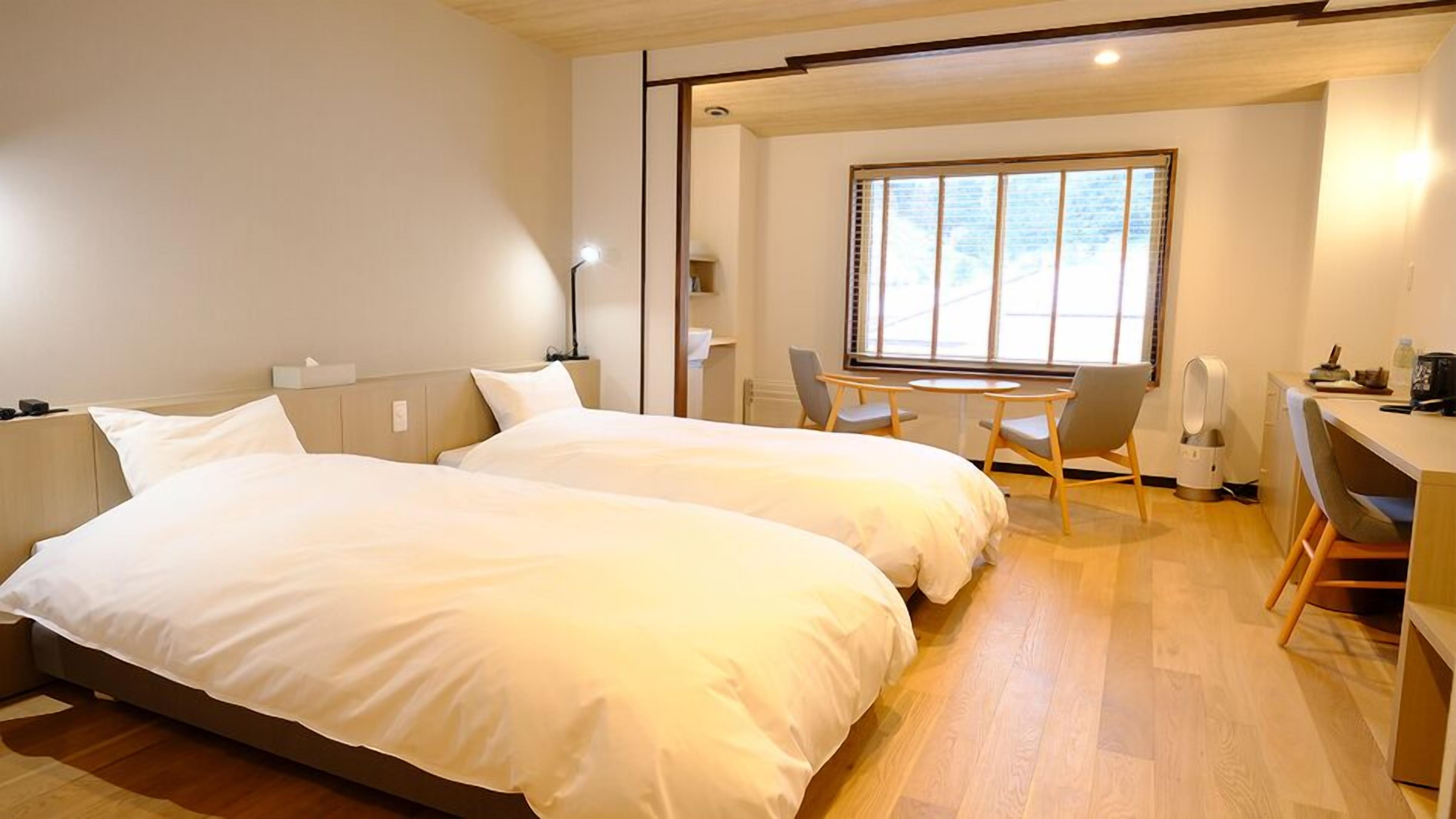 A hotel room with two beds, a desk, a chair, a window, and a radiator.