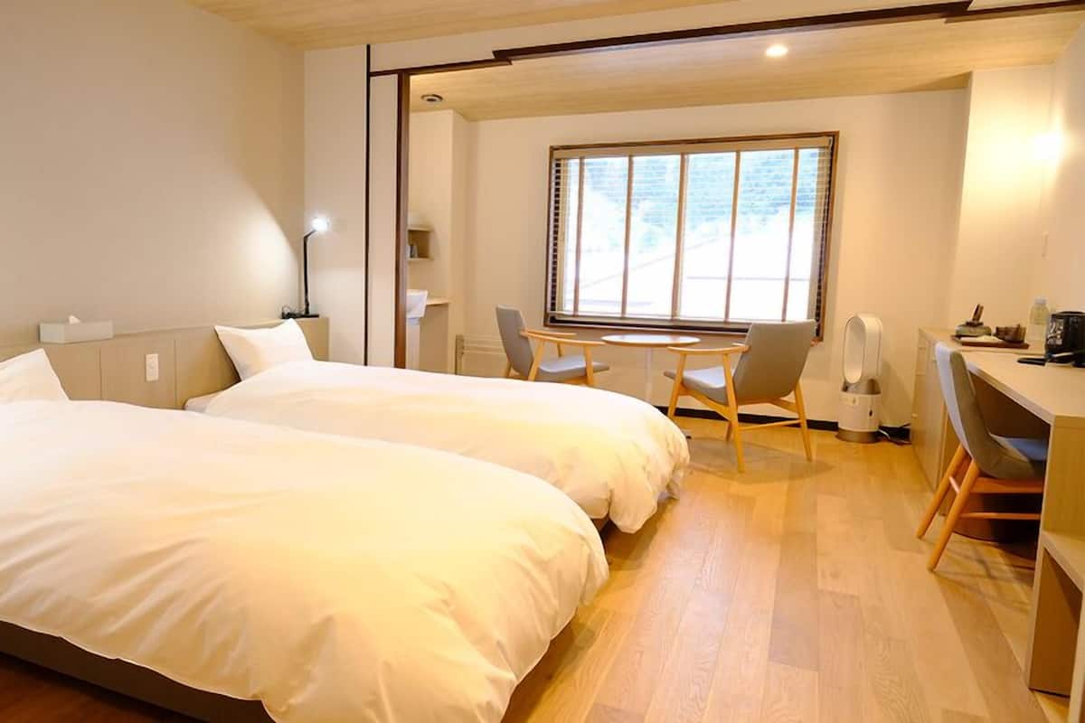 A hotel room with two beds, a desk, a chair, a window, and a radiator.