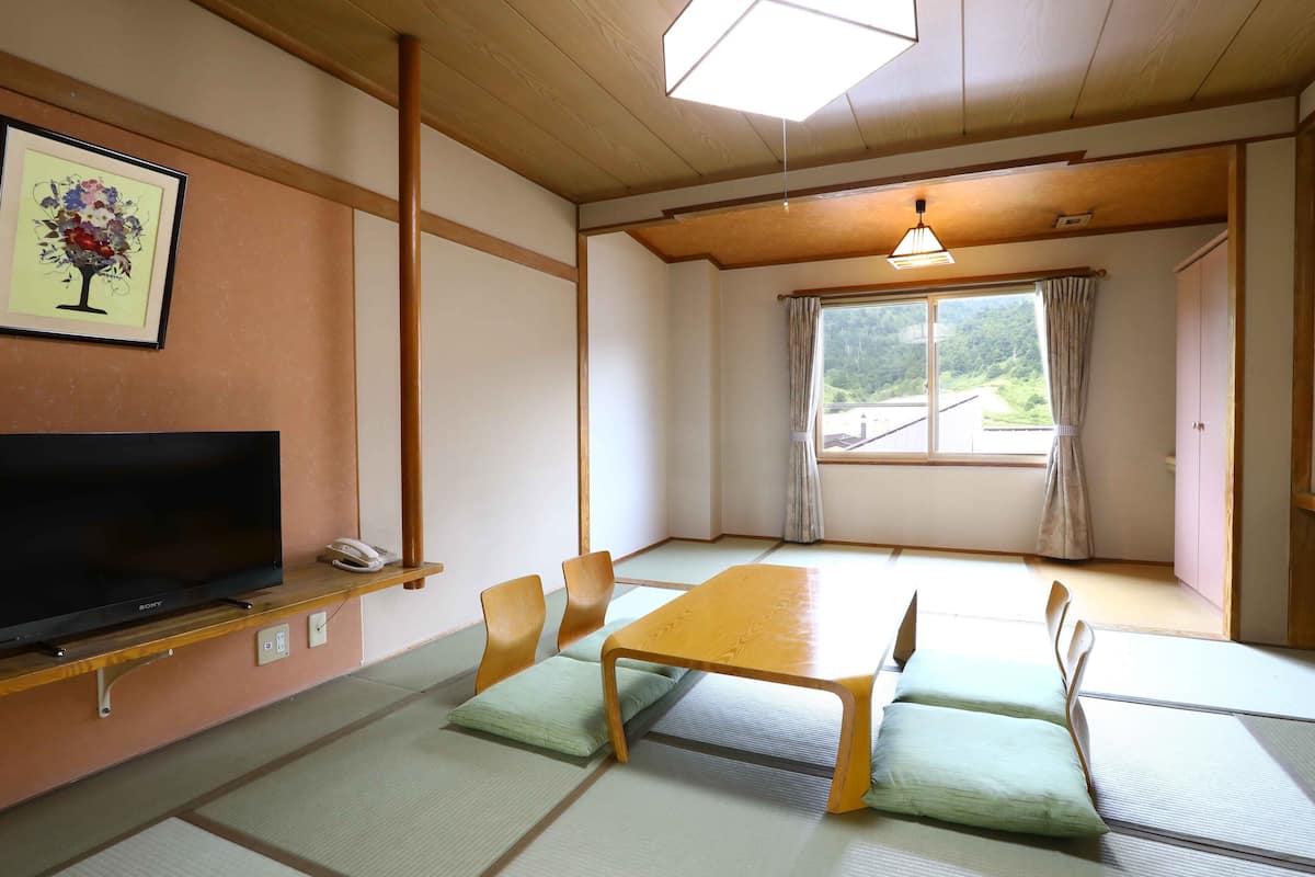 Um quarto tradicional japonês com tatames, uma mesa de madeira baixa e uma televisão em uma prateleira.