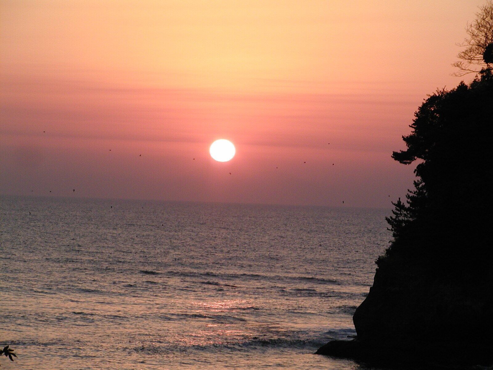 A sunset over a body of water with a silhouette of a cliff.