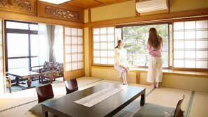 A traditional Japanese room with tatami flooring, a low table, a sofa, and large windows. - Itsuura Kanko Hotel Daikanso (Kitaibaraki)