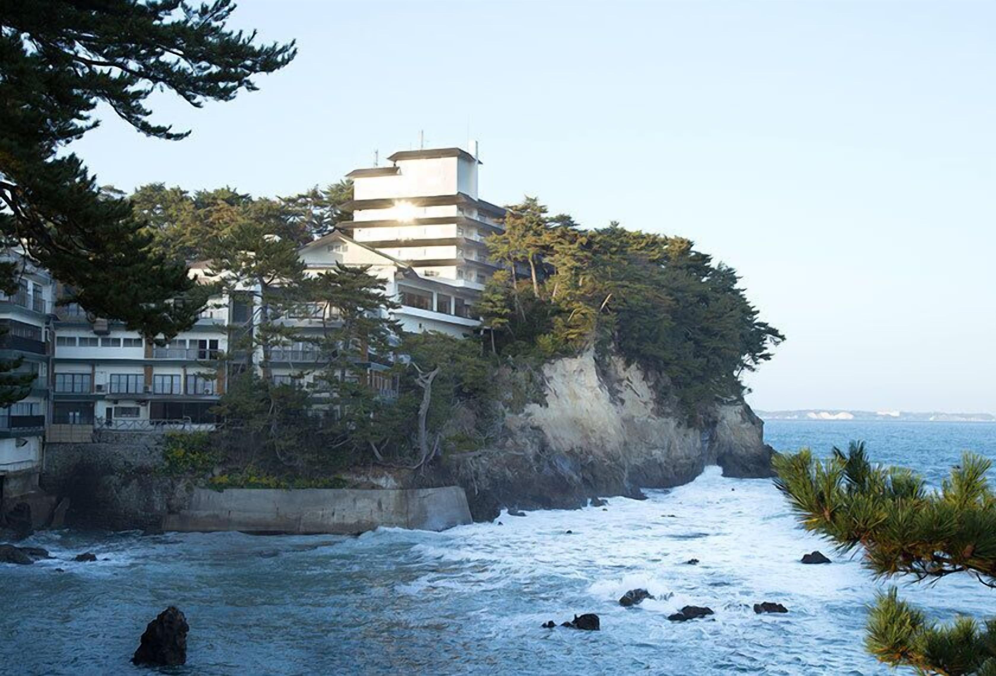 Un bâtiment situé sur la côte, avec plusieurs étages, entouré d’arbres et offrant une vue sur l’océan.
