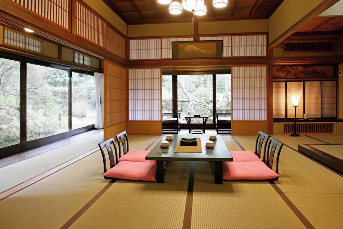 A traditional Japanese room with tatami flooring, a low table, and a ceiling with wooden beams and hanging lights.