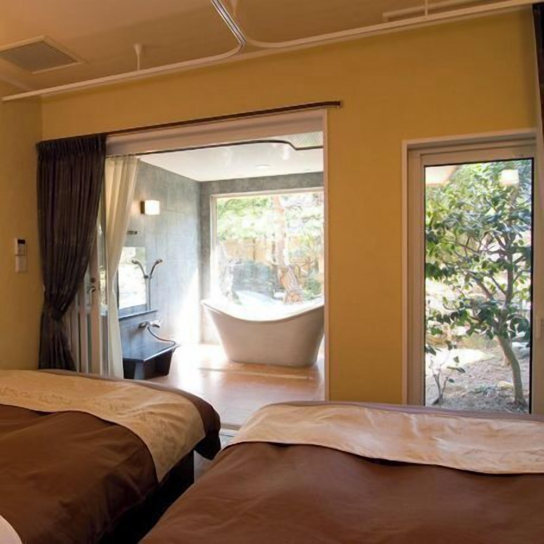 Habitación de hotel con dos camas, una bañera y vistas a la vegetación.