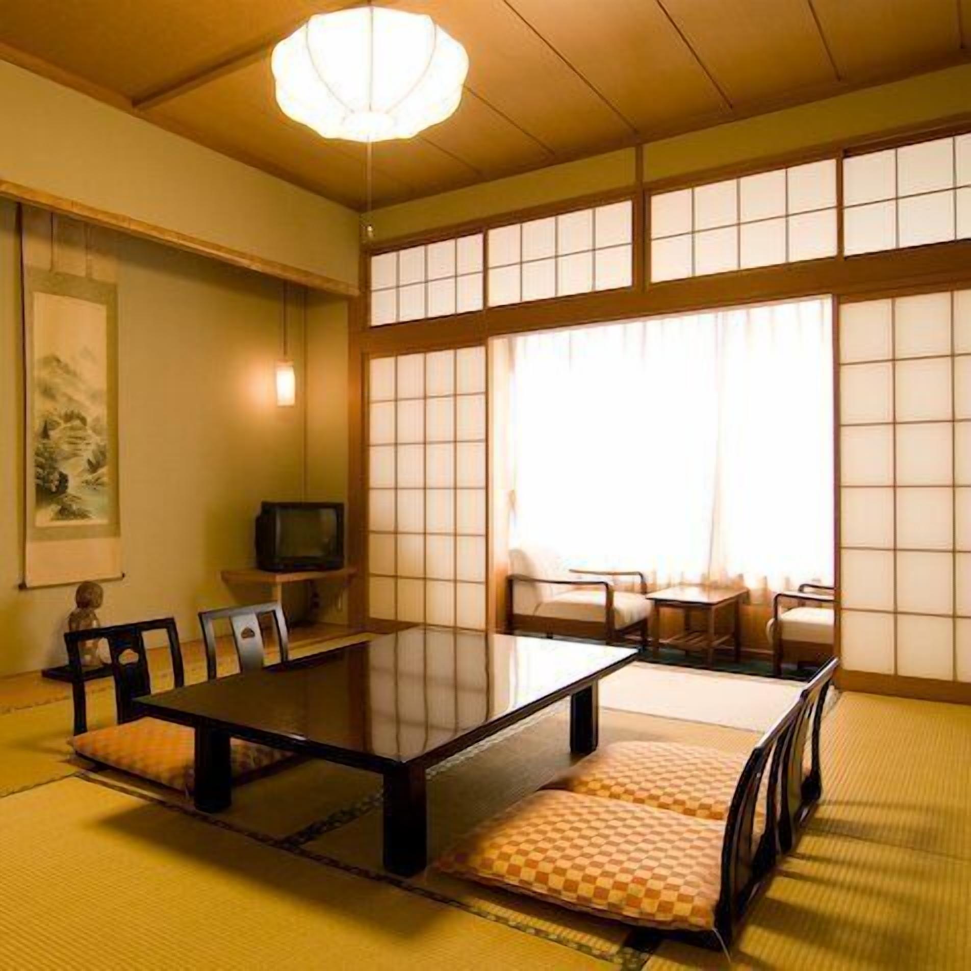 Una habitación tradicional japonesa con suelo de tatami, una mesa baja, sillas y puertas correderas shoji.