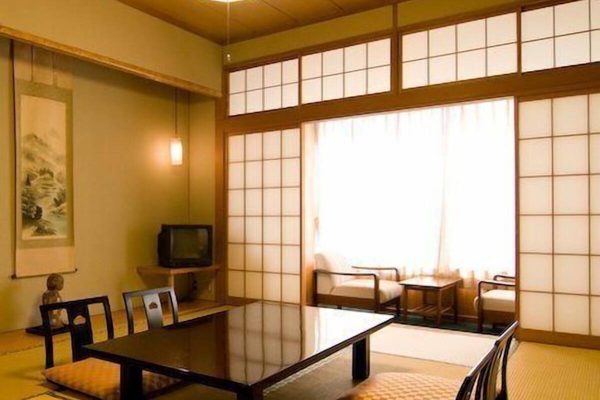 A traditional Japanese-style room with tatami flooring, a low table, chairs, and sliding shoji doors.