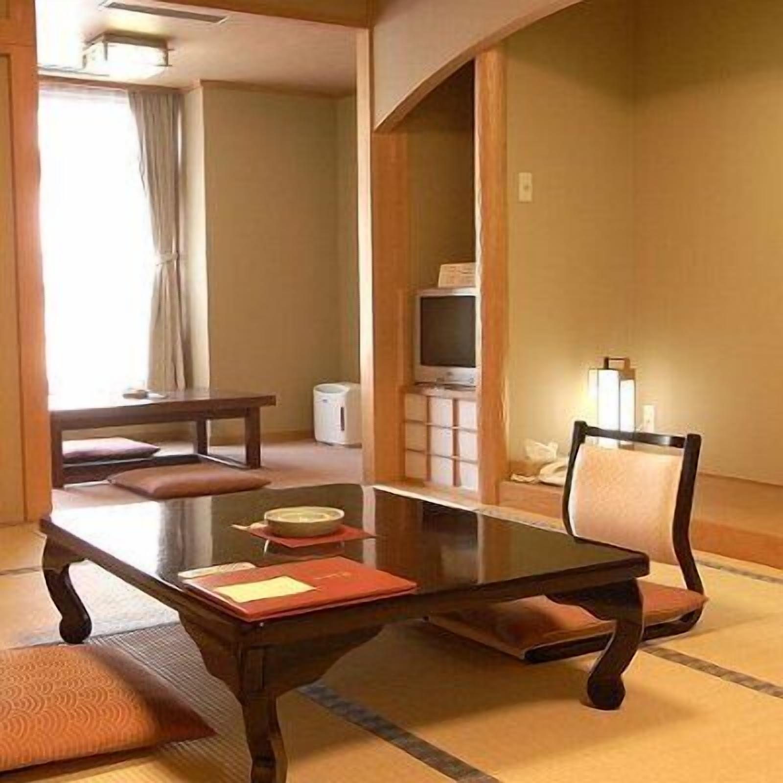 Una habitación japonesa tradicional con suelo de tatami, una mesa baja, una silla, un televisor y un mueble bajo.