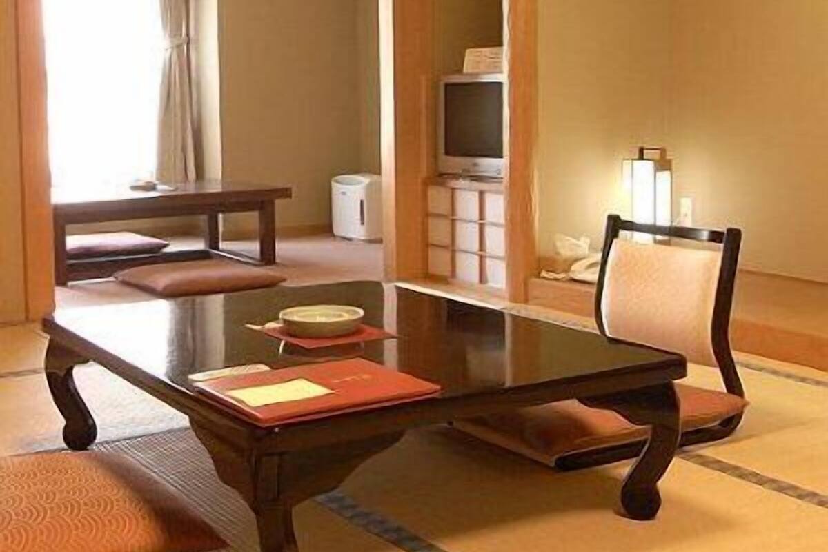 A traditional Japanese room with tatami flooring, a low table, a chair, a television, and a small cabinet.
