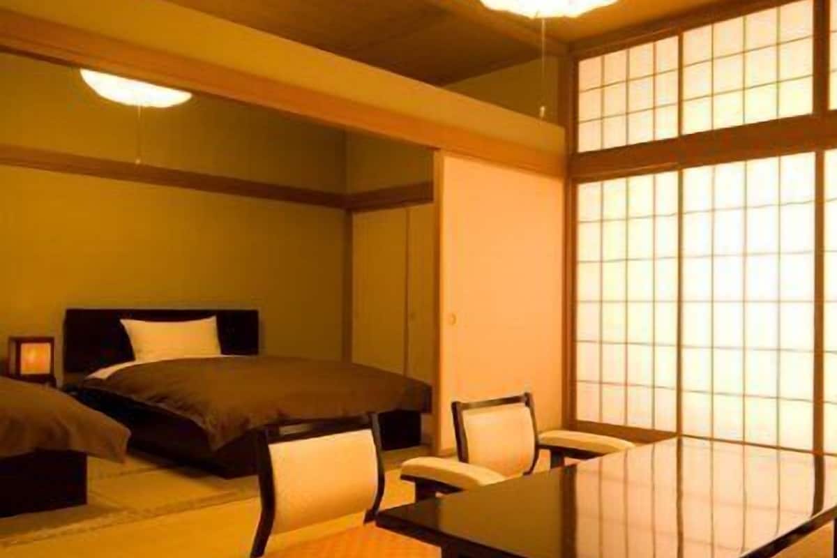 A traditional Japanese-style room with tatami flooring, a low table, and a bed with a dark headboard.