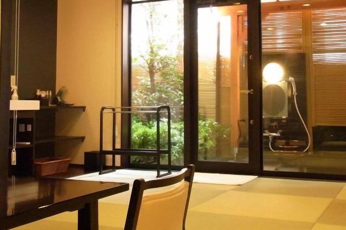 A modern interior with a dining table, chairs, a small kitchen area, and a sliding glass door leading to a garden.