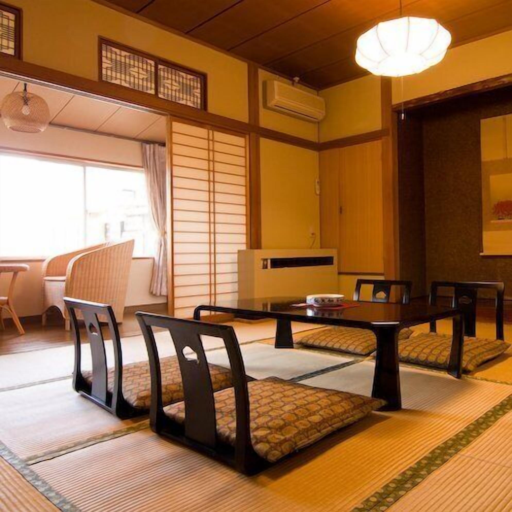 Una habitación japonesa tradicional con suelo de tatami, una mesa baja con sillas y una puerta corredera.