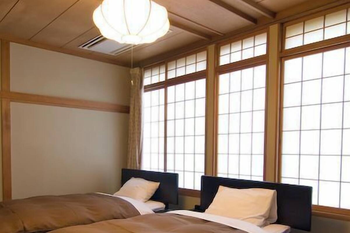 A traditional Japanese-style room with tatami flooring, two low beds with dark headboards, and a shoji screen window.