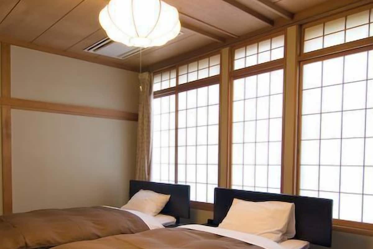 Una habitación tradicional japonesa con suelo de tatami, dos camas bajas con cabeceros oscuros y un ventanal con pantalla shoji.
