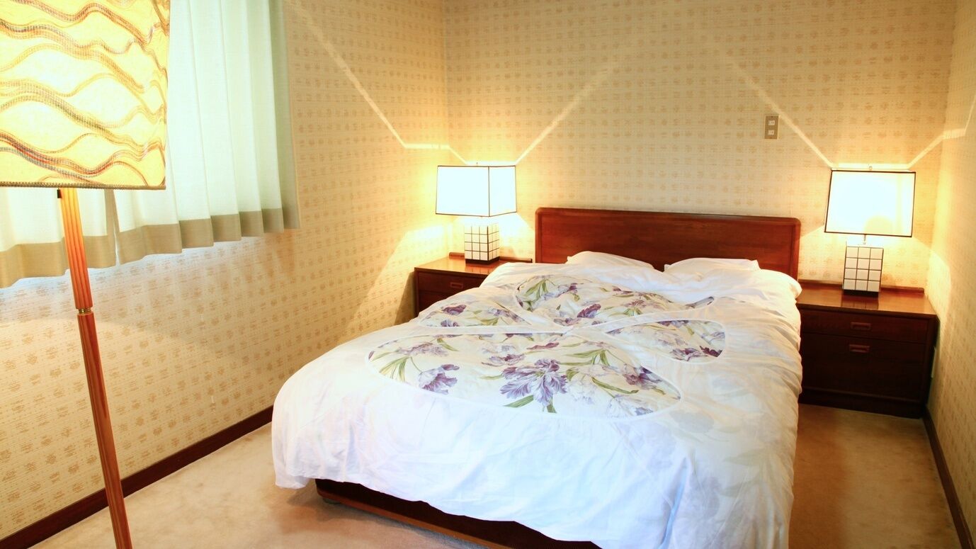A hotel room with a bed, two bedside lamps, a nightstand, and a patterned wall.