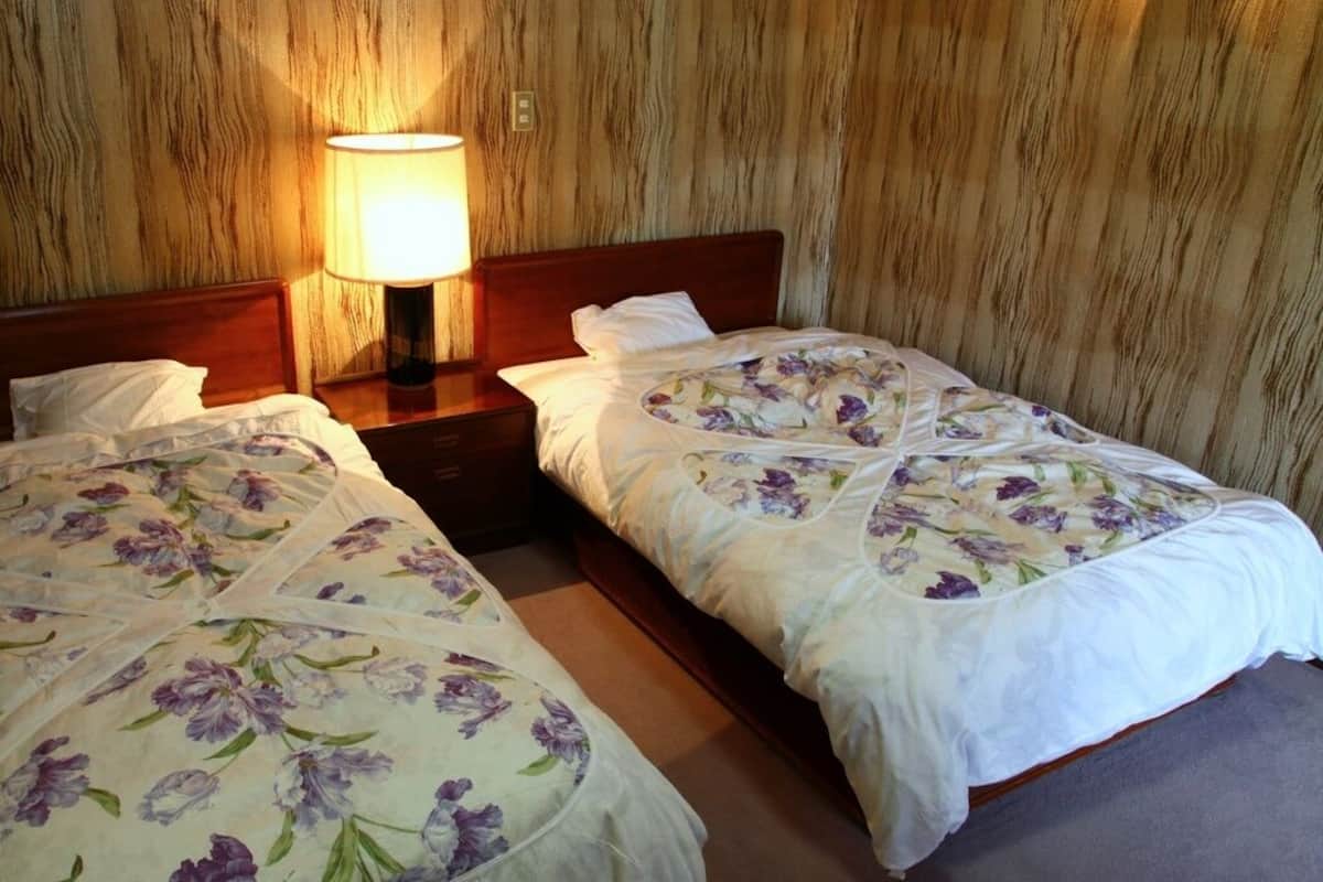 A room with two single beds, wooden headboards, a nightstand with a lamp, and a wooden wall.