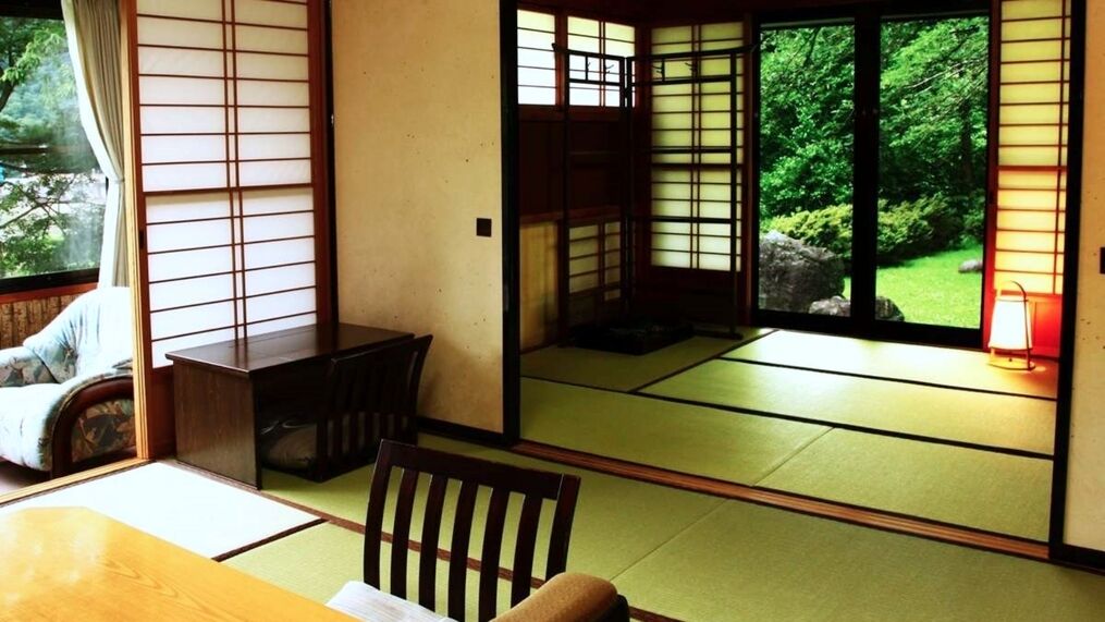 A traditional Japanese room with tatami flooring, sliding doors, a low table, and a chair.