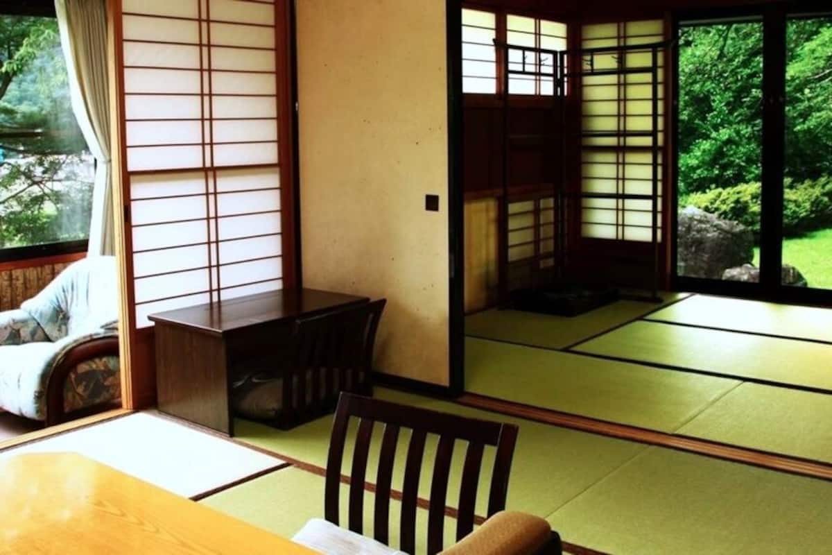 A traditional Japanese room with tatami flooring, sliding doors, a low table, and a chair.