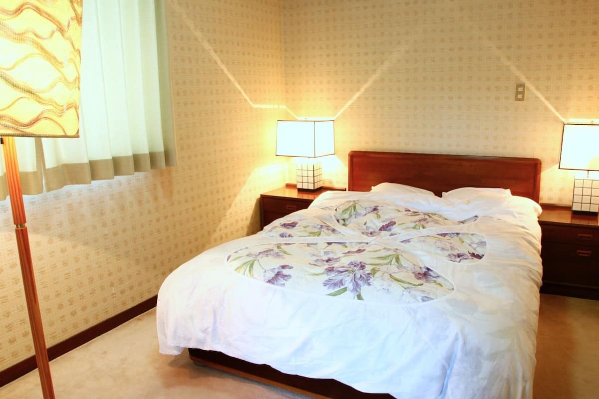 A hotel room with a bed, two bedside lamps, a nightstand, and a wall with patterned wallpaper.