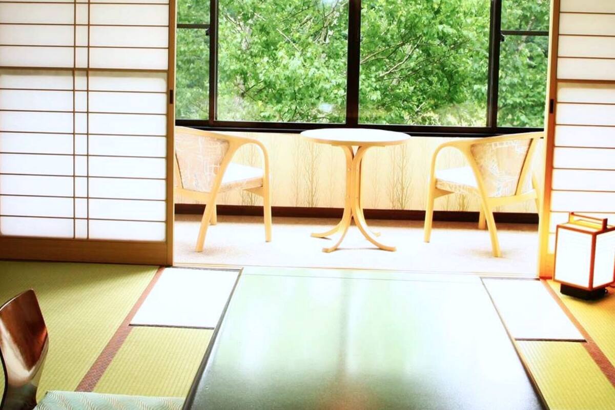 A traditional Japanese room with tatami flooring, a low table, two chairs, and a sliding shoji screen.
