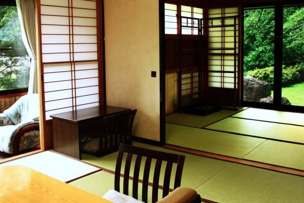 A traditional Japanese room with tatami flooring, sliding doors, and a view of greenery outside.