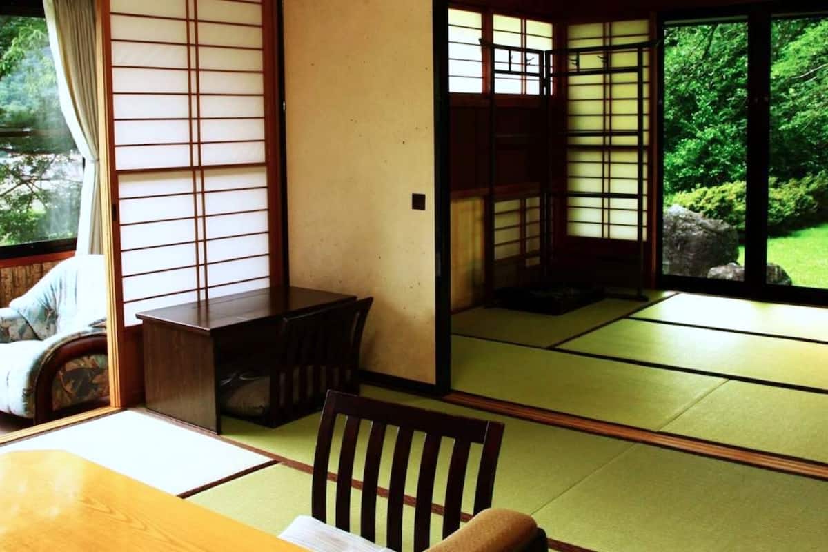 A traditional Japanese room with tatami flooring, sliding doors, and a view of greenery outside.