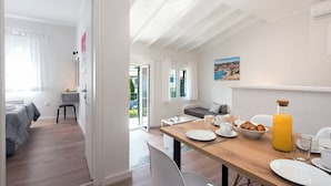 Una habitación moderna con una mesa de madera dispuesta para el desayuno, un sofá y una cama con vistas al exterior.