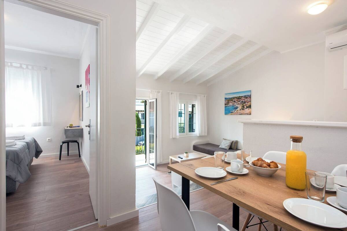 A modern room with a wooden dining table set for breakfast, a sofa, and a bed with a view to the outdoors.