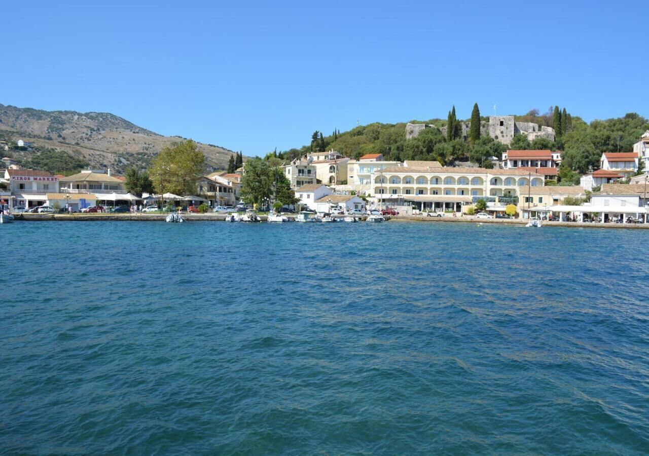 A coastal town with buildings along the waterfront, a clear blue sky, and a hilly backdrop.
