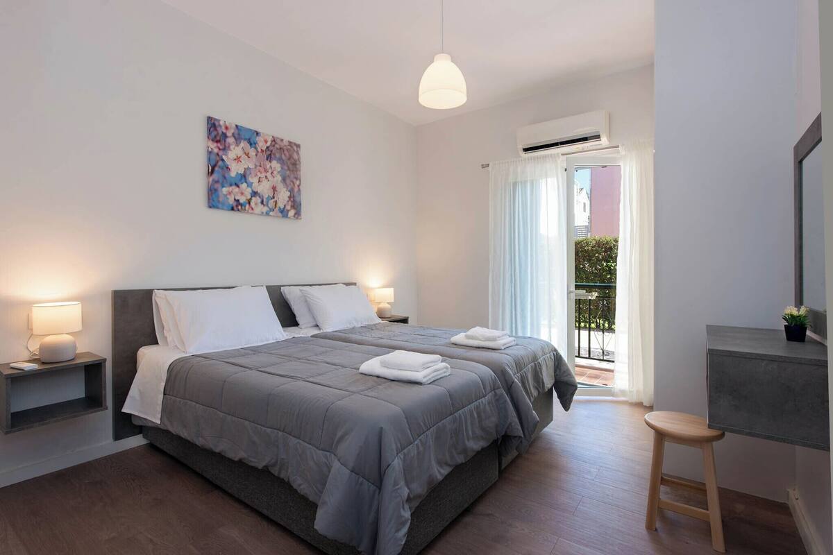 A modern bedroom with a large bed, bedside lamps, a desk, and a balcony with curtains.