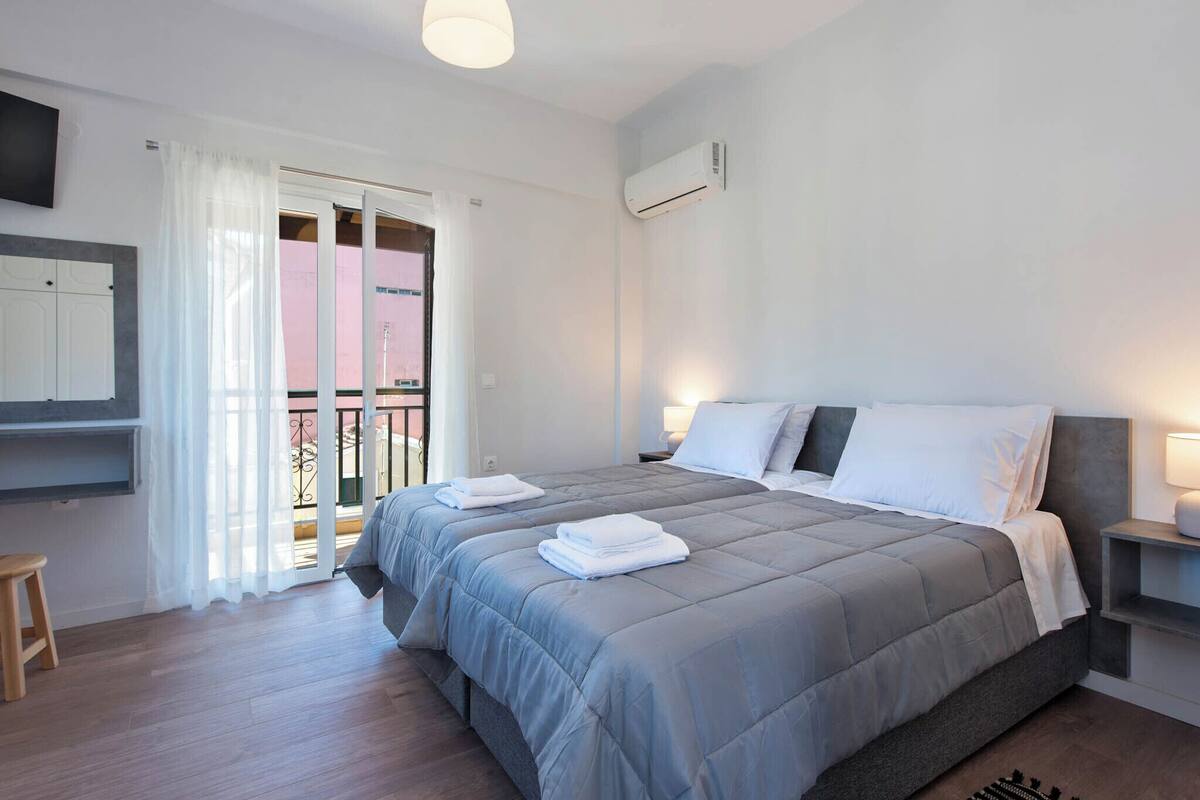 A bedroom with a bed, a TV, a window with curtains, and an air conditioning unit.
