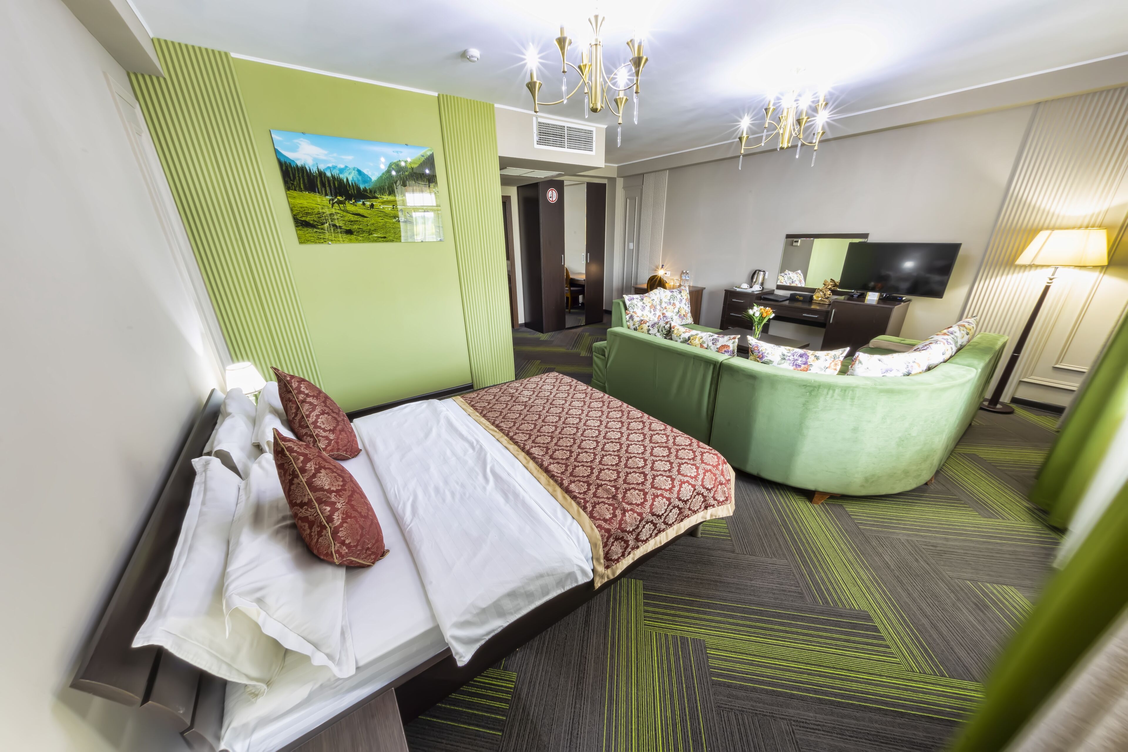 A hotel room with a bed, a desk, a chair, a TV, and a lamp.